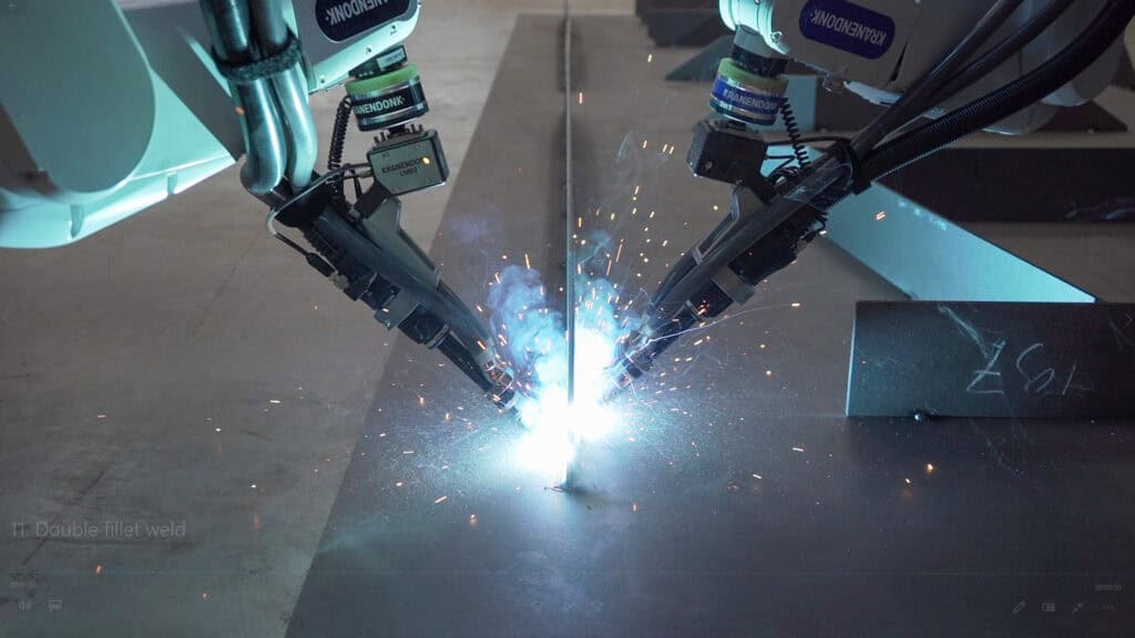 Two KRANENDONK robotic welding arms performing a synchronized double fillet weld on a vertical seam.